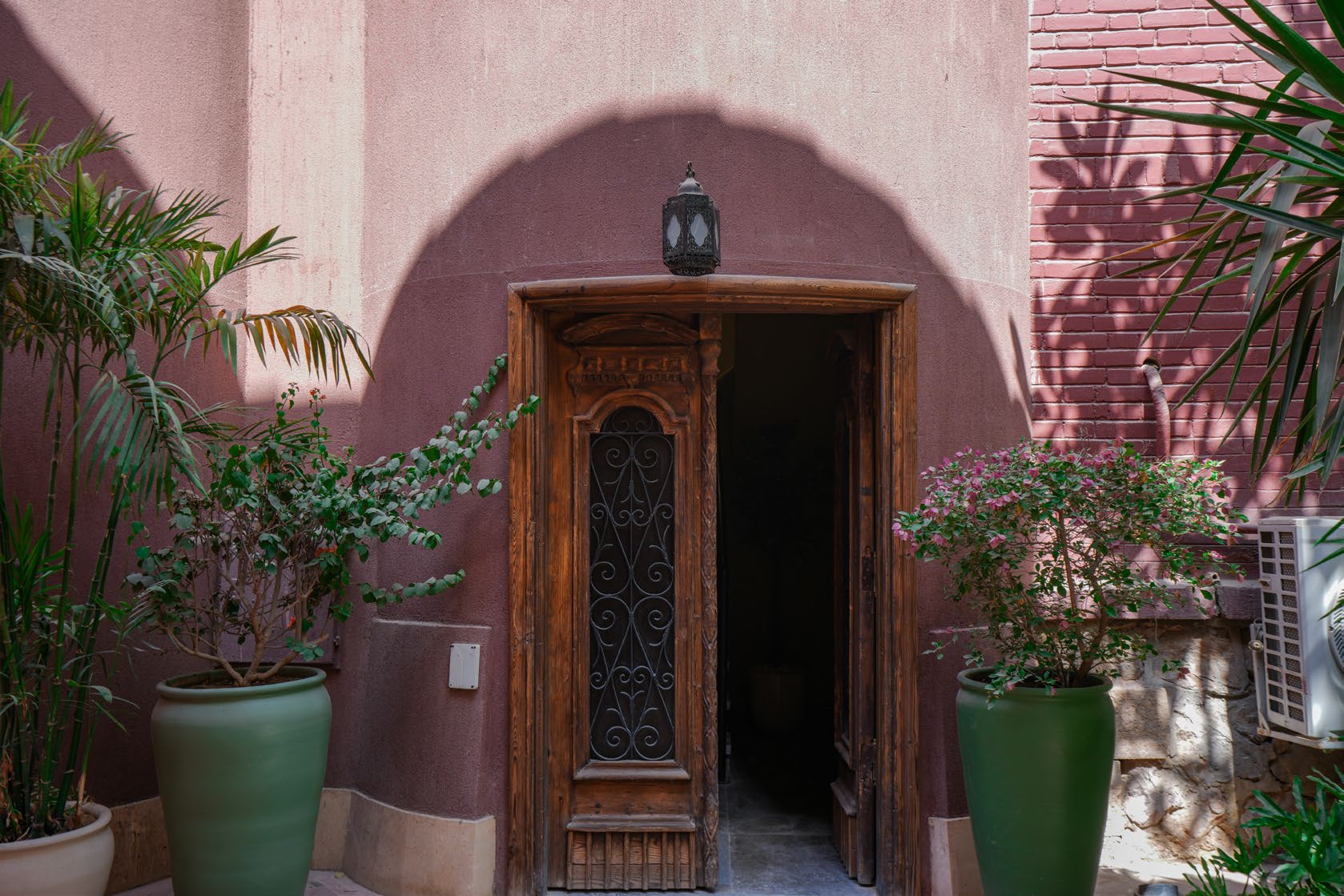 The rose-pink entrance wall of Villa Atouta with a carved wooden door and potted palms